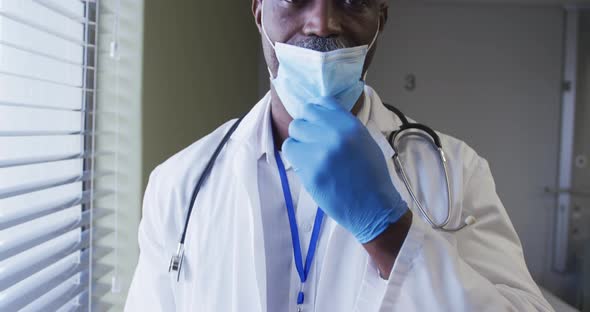 Portrait of smiling african american male doctor wearing face mask standing in hospital room