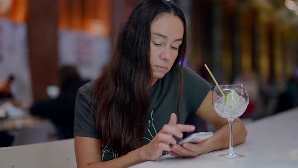 Adult Woman with Cocktail in Bar is Using Smartphone for Viewing Social Networking