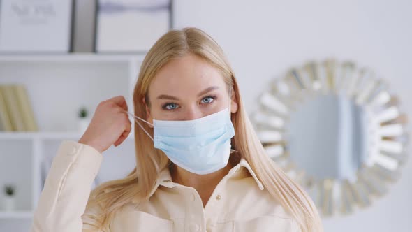 Young attractive girl taking off the medical blue mask. Beautiful smiling woman without medical mask