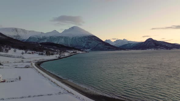 Polar night has colorful sky, windy conditions over ocean with snowy mountains