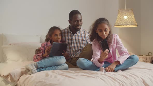 Father with Kids Resting on Bed with Gadgets