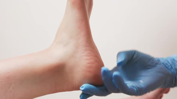 Pedicurist in blue medical gloves massages the female foot's heel