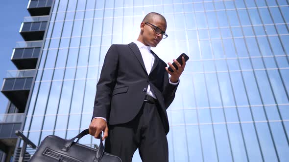 Happy Smiling Businessman Wearing Black Suit And Using Smartphone Near Office