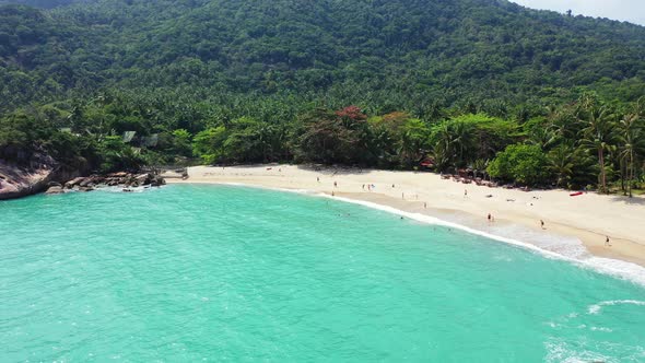 Foamy waves lapping on the sandy coast. Secluded tropical beach surrounded by forested hills and roc