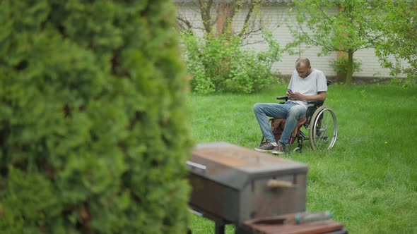 Extreme Wide Shot Portrait of African American Paralyzed Man in Wheelchair Sitting in Summer Garden