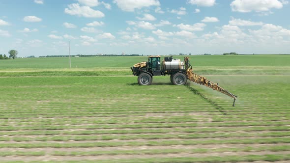 Side aerial, tractor spraying pesticide and herbicides during summer day. Farm machinery spraying in