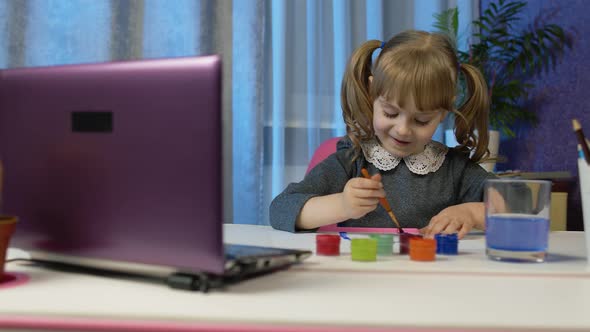 Girl Enthusiastically Drawing with Brushes and Paints Using Laptop at Home Distance Education