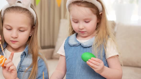 Two Girls with Rabbit Ears Celebrate Easter and Decorate Eggs with Paints