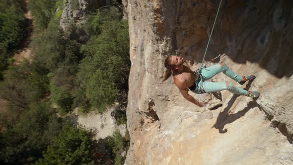 Young Athletic Man Rock Climber with Long Hair Climbs on the Overhanging Cliff