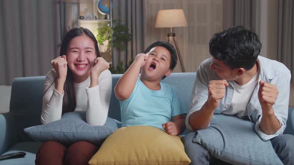 Asian Family Celebrating While Watching Tv Together Sitting On A Sofa In The Living Room At Home