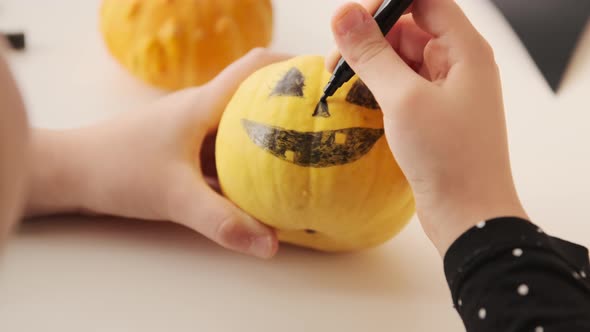 Kid preparing for holiday Halloween. Child hands drawing scary face on pumpkin