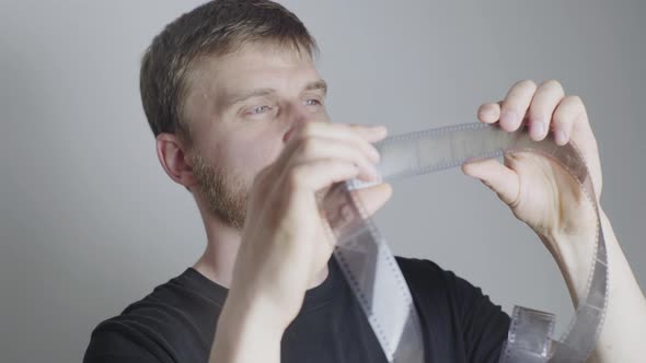 a Blond Man with a Beard a Photographer Examines a Film on a White Background