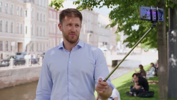 Man Blogger Using Selfie Stick and Smartphone Making Video for Internet Blog on Street