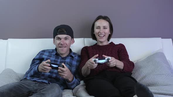Excited girl and young man sitting on couch and playing video games on console