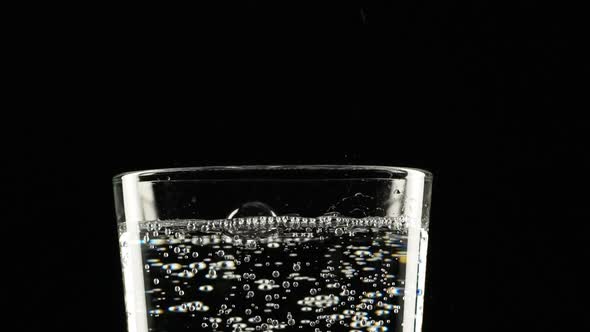 Footage in Slowmotion of Top of Glass with Clear Sparkling Water Standing on Black Background
