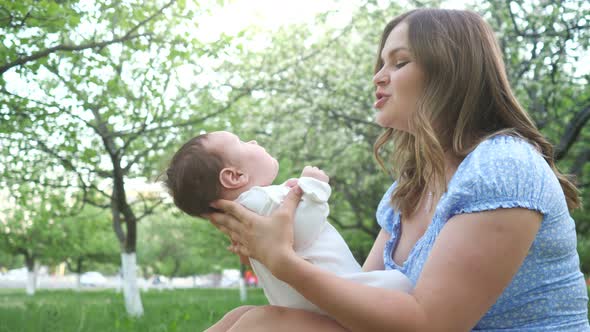 Mother with Long Loose Fair Hair Plays with Kid on Grass