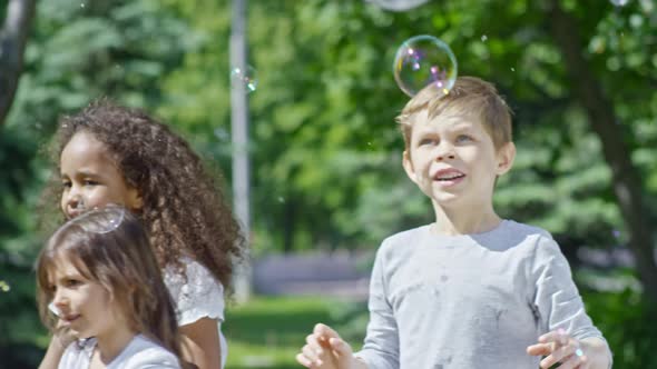 Smiling Boys and Girls Playing with Bubbles at Summer Day