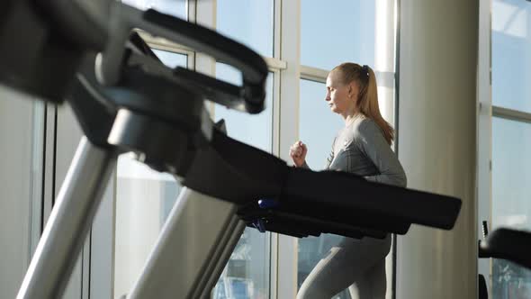 Attractive woman of middle age is running on tread mill in sport gym