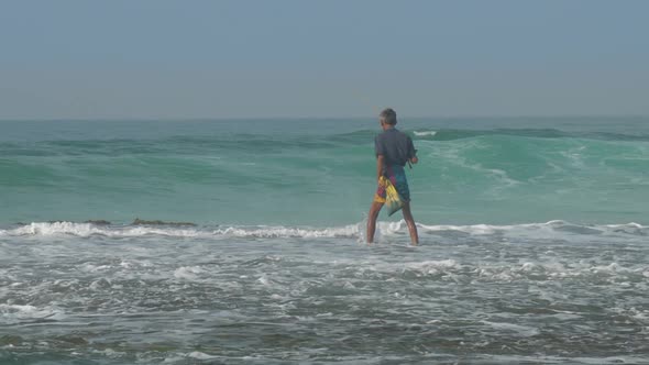 Fisherman Walks Along Water Surf Edge at Foaming Ocean Waves