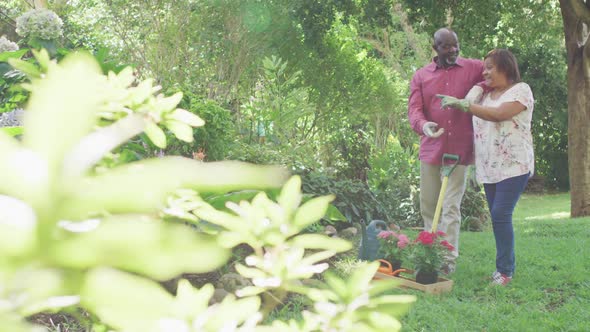 Animation of happy african american senior couple planting flowers in garden