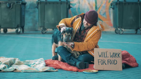 A Beggar is Feeding His Dog While Sitting on the Ground