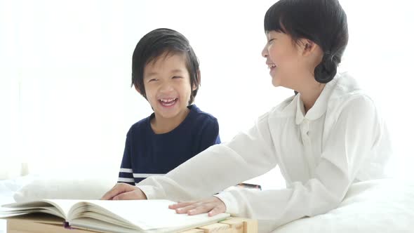 Cute Asian Children Reading A Book On White Bed