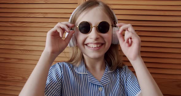 Cute Girl with Round Sunglasses and Wireless Headphones Listening to Music