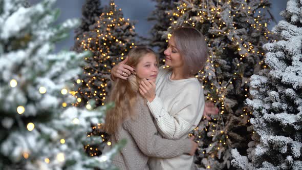 Mom and daughter hug and smile at each other standing in a snowy forest