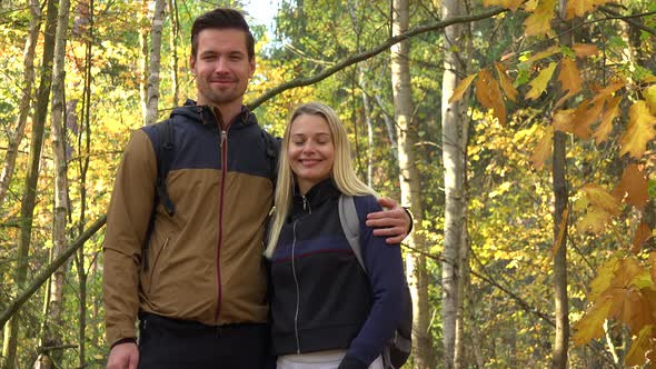 A Hiking Couple Smiles at the Camera in a Forest on a Sunny Day