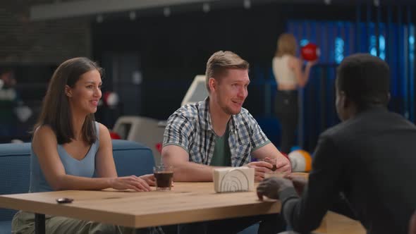 A Multiethnic Group of Friends Sits at a Table Together in a Bowling Alley and Talks