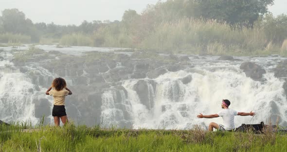 Woman is filming the gorgeous Victoria Falls and a man is sitting on a rock, 4k