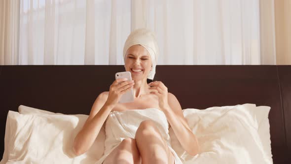 Young Happy Woman with Blonde Hair Smiling and Using Cellphone While Sitting on