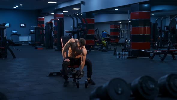 Male athlete with perfect abs trains in modern gym with dumbbells. Slow motion.