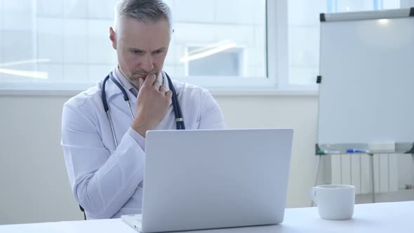 Pensive Doctor Thinking and Working on Laptop