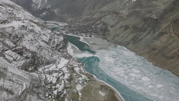 Aerial Flying Over Frozen Valley With Turquoise River Running Through With Tilt Up View Of Snow Capp