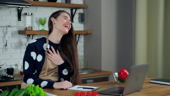 Laughing woman study online video call laptop listens tells teacher in kitchen