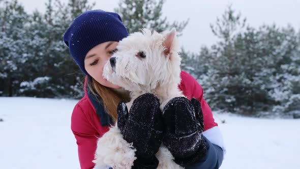 Attractive woman in hat and warm mittens holding west highland white terrier