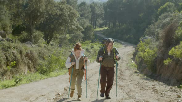 Two Girls Walking Up Wide Dirt Road with Trekking Poles