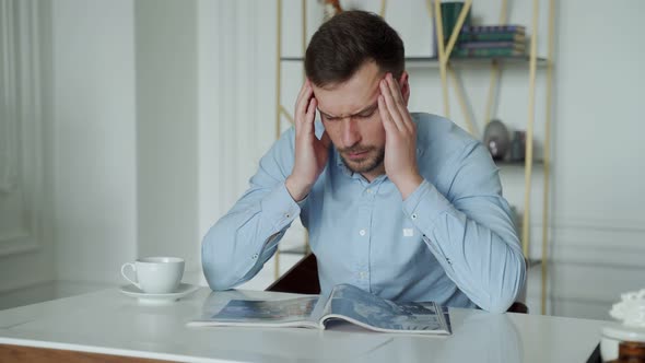 A Sad Young Man with a Headache is Sitting at a Desk in the Office