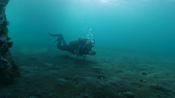 A Scuba Diver in a Diving Suit with the Necessary Equipment Swims Up to a Beautiful Coral Reef