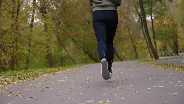 Lower body of woman jogging on road in autumn