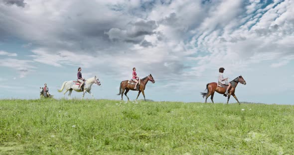 Four Active People Riding Horses on a Sunny Outdoor Wild Green Outdoor field, Side Follow Wide Shot