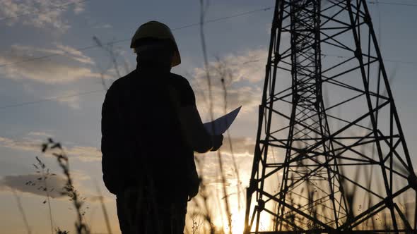 Silhouette of Engineer Standing on Field with Electricity Towers. Electrical Engineer with High