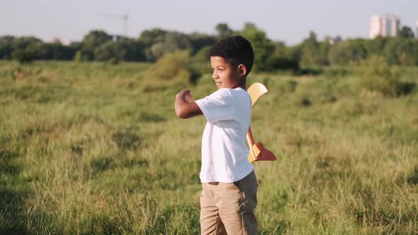 African Boy in a White Shirt with a Plane in Hands on Field