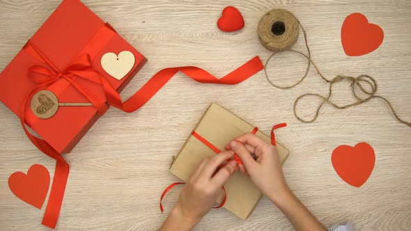 Person Packing Craft Valentines Gift Box on Wooden Background, Preparation