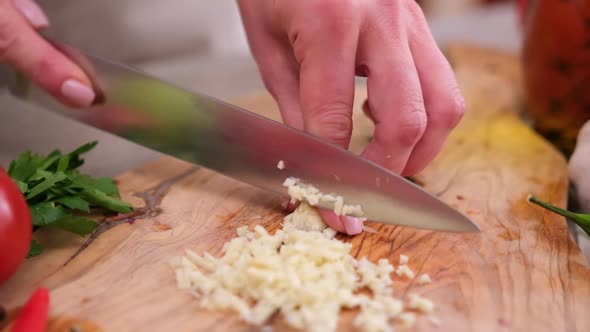 Woman Slices Garlic on a Kitchen Board Using a Knife