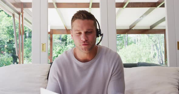 Portrait of caucasian man using phone headset talking looking at the camera while sitting on the cou