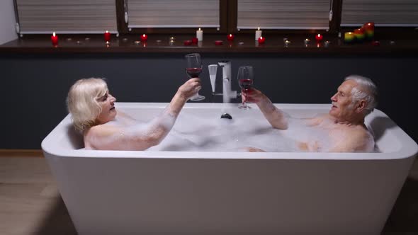 Senior Couple Grandfather and Grandmother Is Taking Foamy Bath Drinking Red Wine in Luxury Bathroom