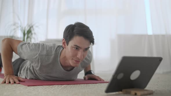 Handsome Young Man in a Gray T-Shirt and Black Shorts Does Sports at Home Online. Handsome Man