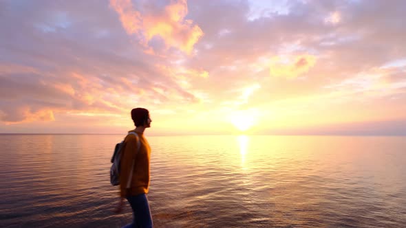 Young GoodLooking Woman Wearing Red Hat and Yellow Sweater and Slowly Approaching Ocean